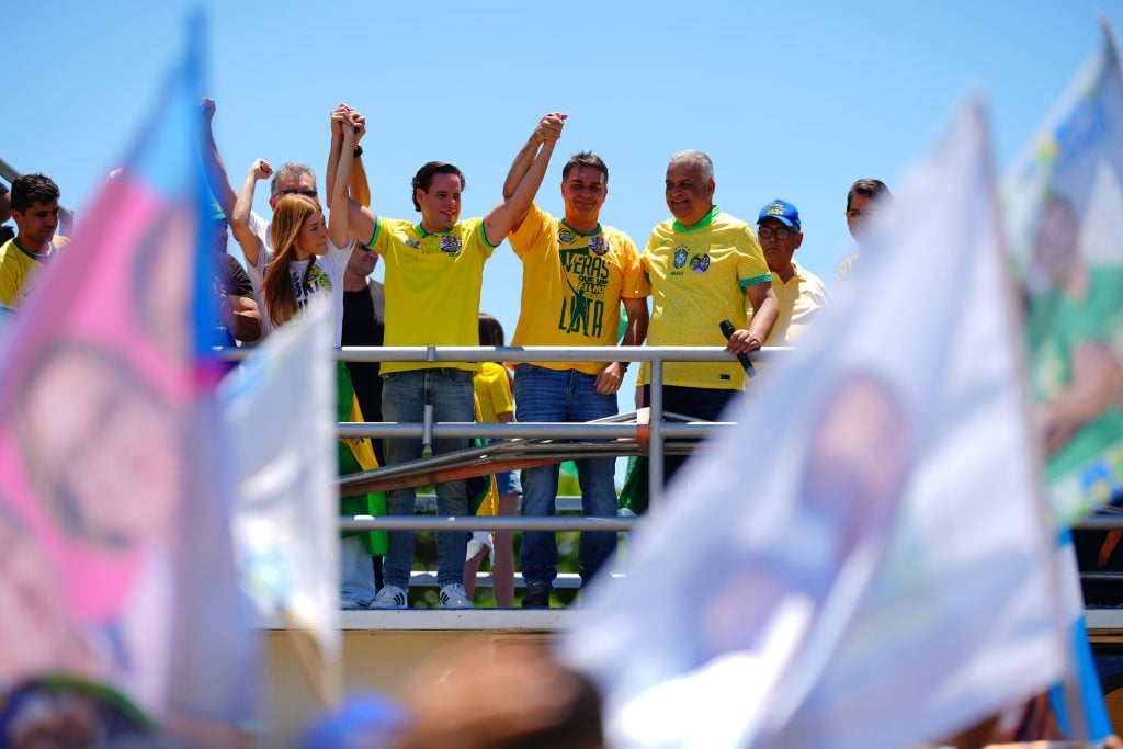 Flávio Bolsonaro ergue as mãos ao lado de aliados no palanque em Aracaju