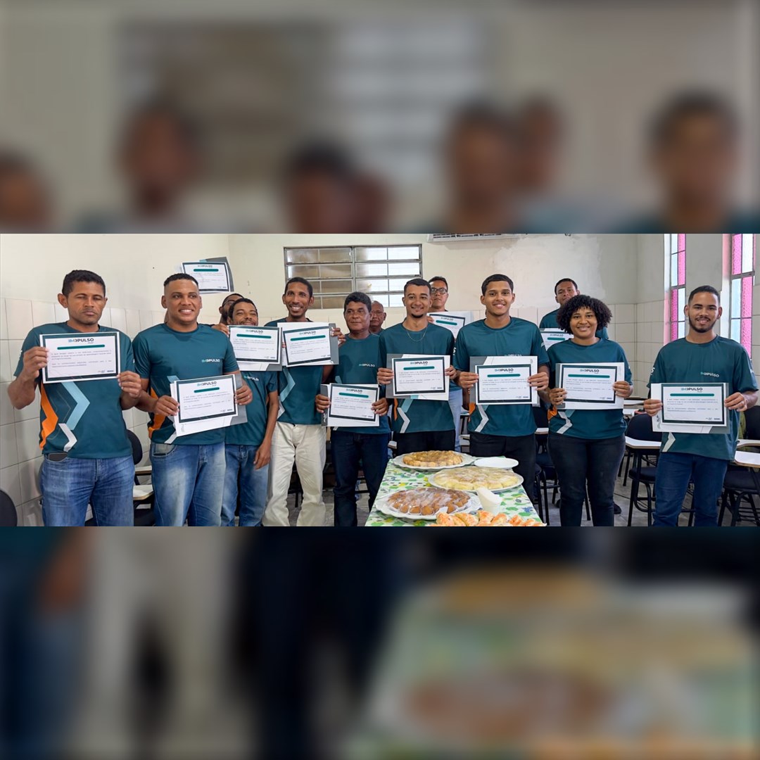 Grupo de alunos com camisas verdes segura certificados em uma sala de aula, ao lado de uma mesa com salgados