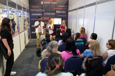 Três palestrantes falam ao microfone para plateia sentada em sala de workshop com painel da Aracaju Beauty Hair e da Dreams