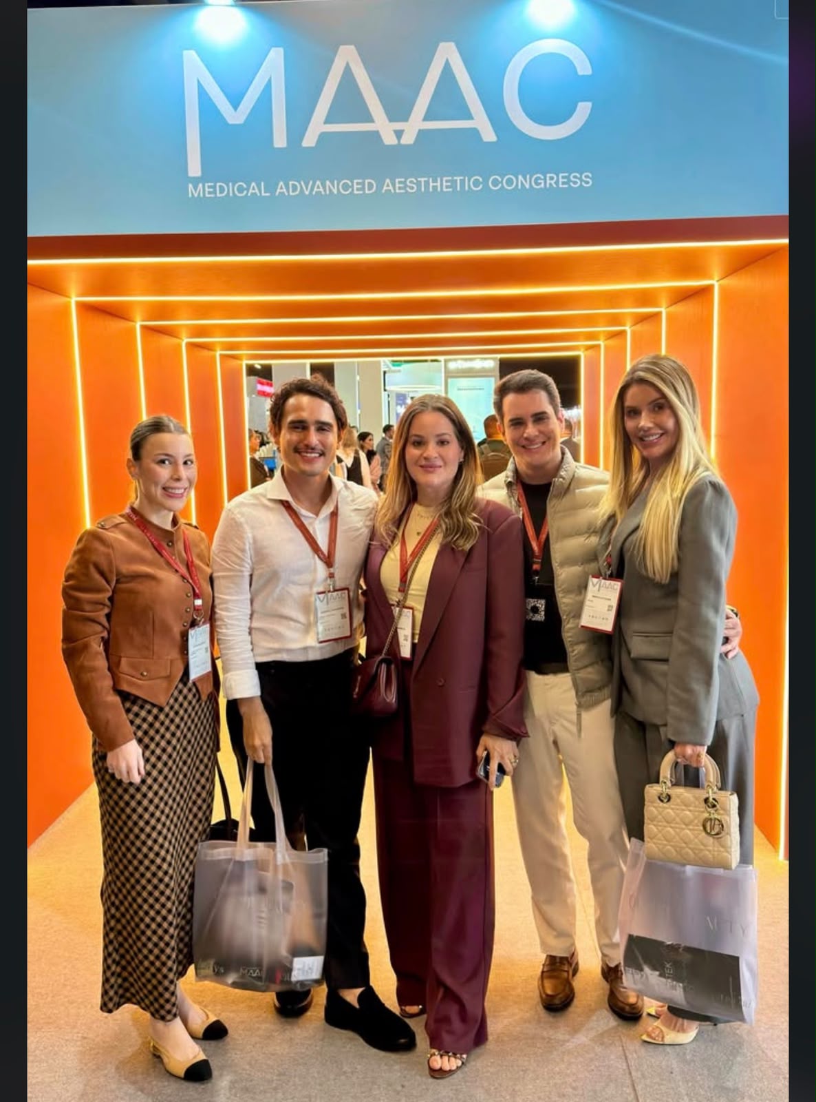 Cinco médicos com crachás posam diante da entrada iluminada em laranja do MAAC, Medical Advanced Aesthetic Congress