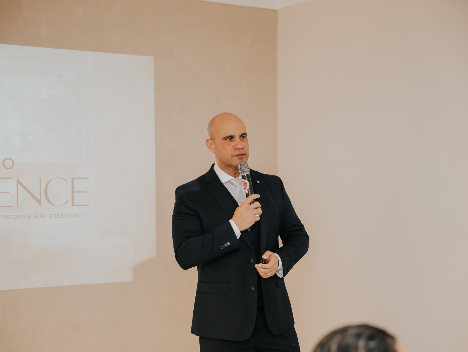 Dr. Adelmo Alves, de terno escuro, fala ao microfone diante de uma projeção com a marca do Instituto NeoEssence