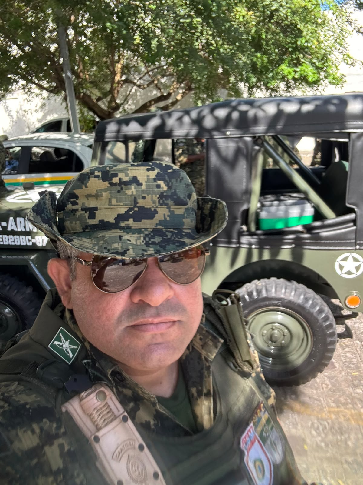 Veterano do GVEB, com chapéu camuflado e óculos escuros, posa ao lado da Jeep Willys histórica usada no desfile