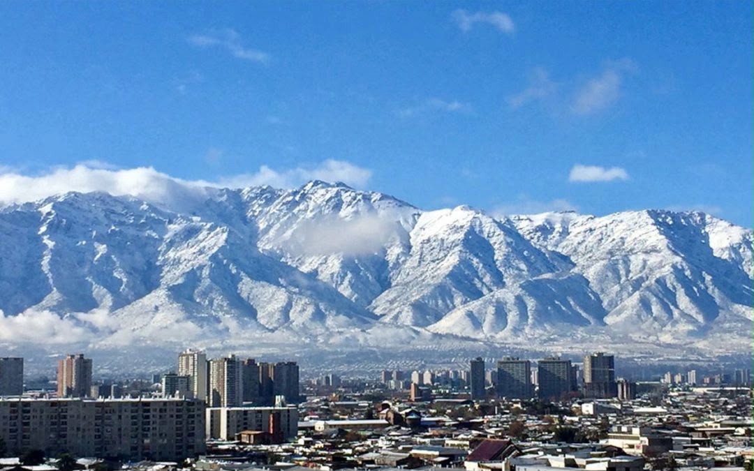 Sergipanos podem parcelar viagem para o inverno de 2027 ainda em 2026 1 Vista da cidade de Santiago, no Chile, com prédios em primeiro plano e a Cordilheira dos Andes coberta de neve ao fundo, sob céu azul